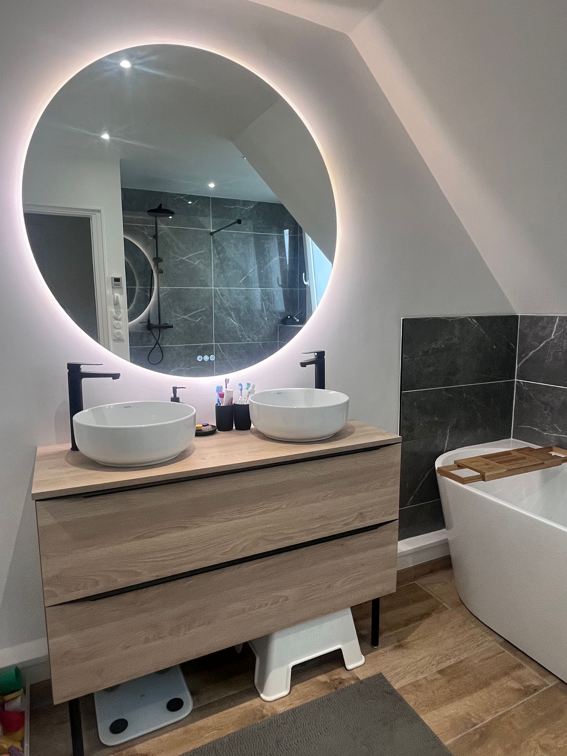 Salle de bain moderne avec miroir rond, double vasque et baignoire.