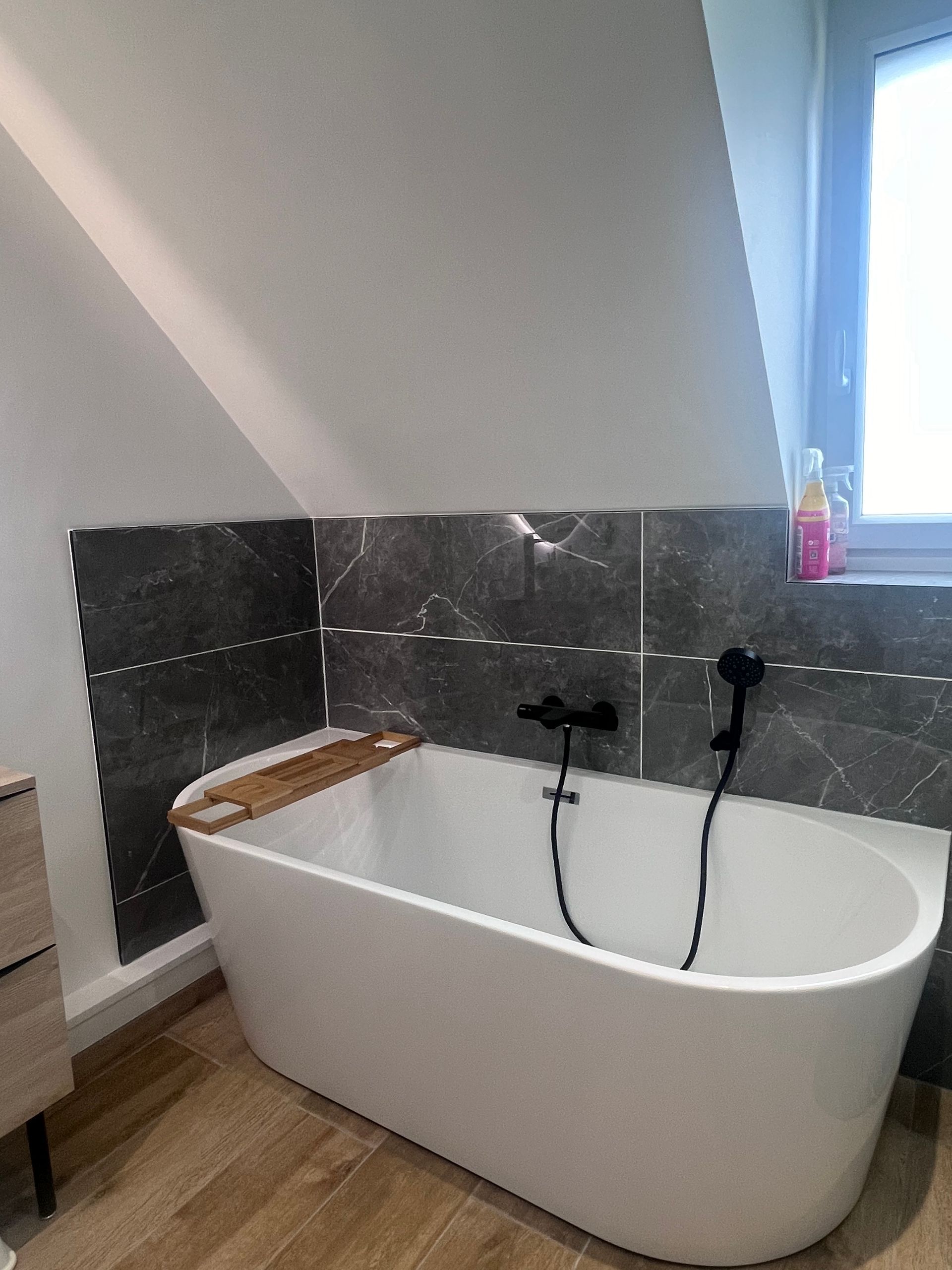 Baignoire blanche avec accessoires noirs sur fond de carrelage en marbre gris dans une salle de bain moderne.