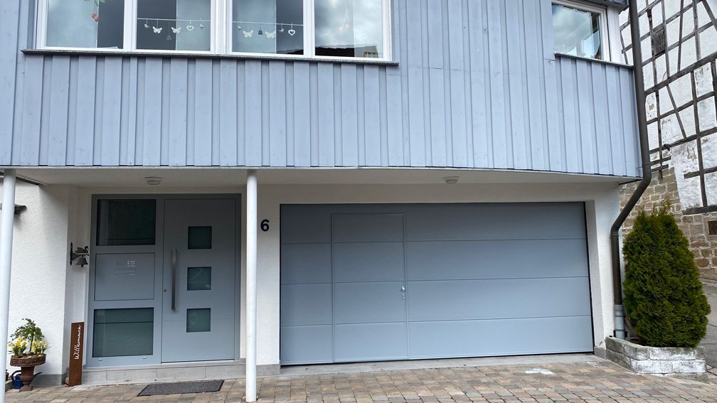 Die Vorderseite eines Hauses mit einem blauen Garagentor und einer weißen Tür.