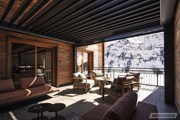 Ein Balkon mit Sofa, Stühlen, Tischen und Blick auf einen schneebedeckten Berg.