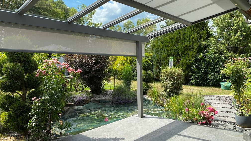 Eine Terrasse mit einem Baldachin darüber und einem Teich im Hintergrund.