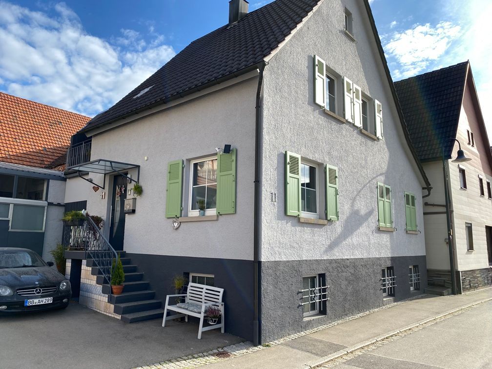 Ein weißes Haus mit grünen Fensterläden und einem davor geparkten Auto.