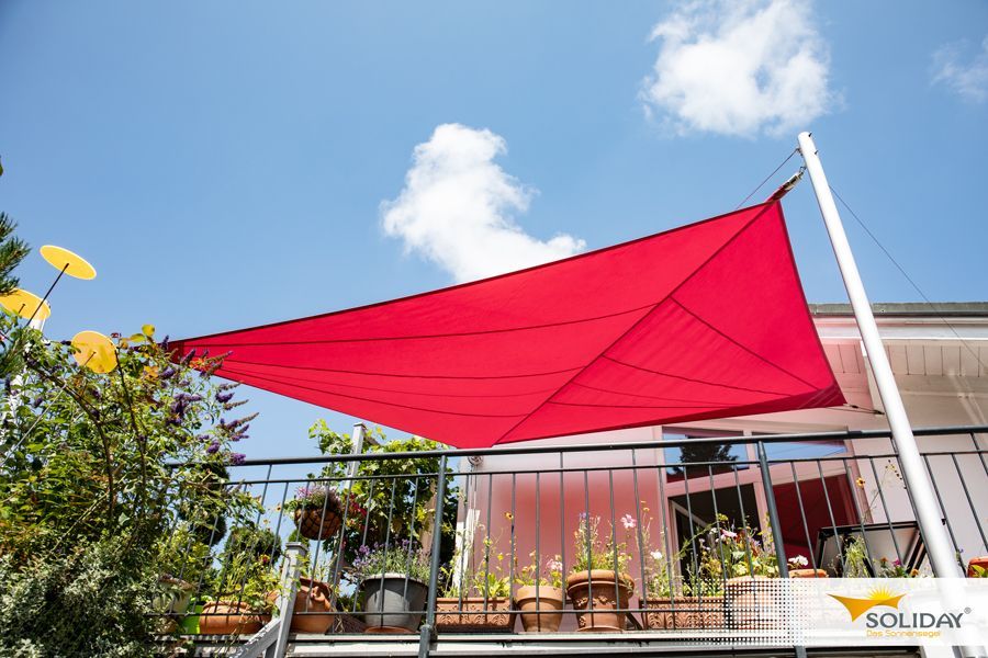 Auf einem Balkon steht ein roter Regenschirm.