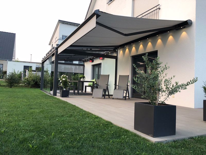 Eine Terrasse mit Tisch und Stühlen unter einer Markise vor einem Haus.