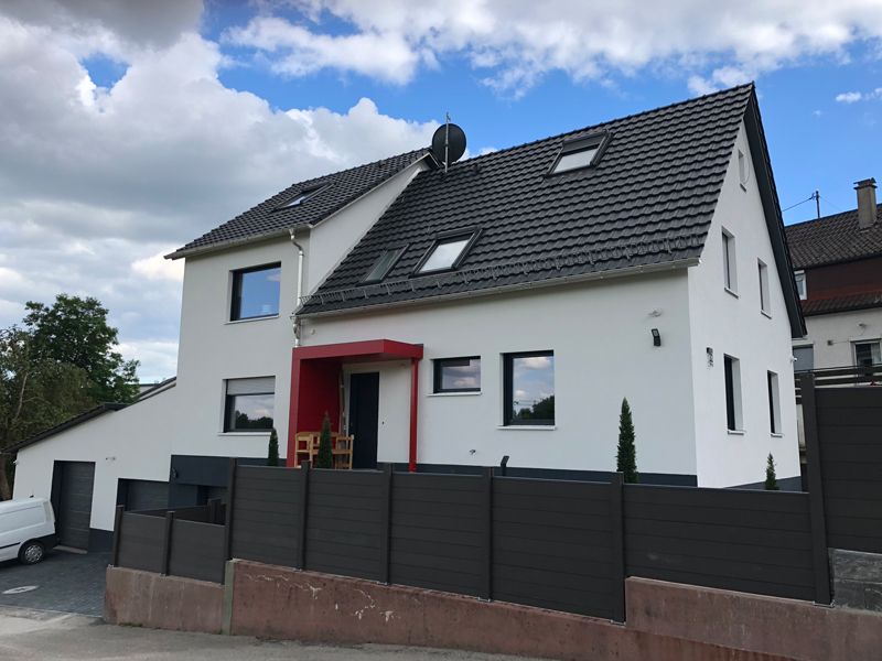 Ein weißes Haus mit einem schwarzen Dach und einem schwarzen Zaun