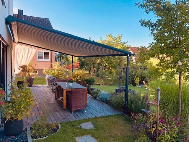 Eine Terrasse mit Tisch und Stühlen unter einem Baldachin in einem Garten.