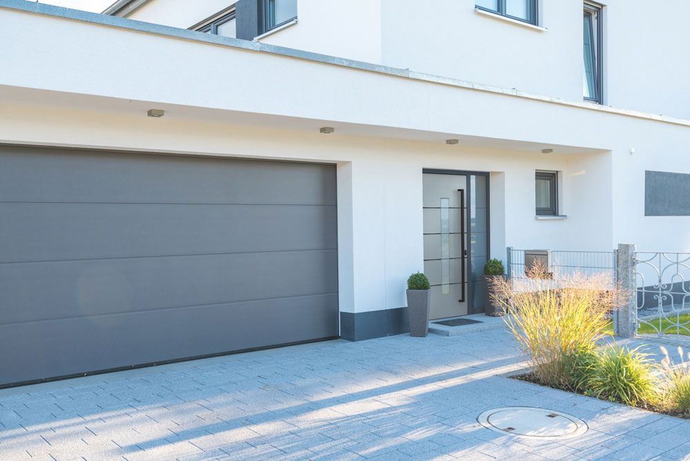 Ein weißes Haus mit einem grauen Garagentor und einer schwarzen Tür.