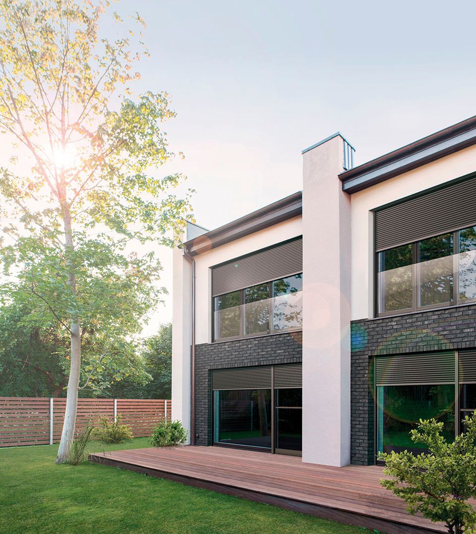 Ein großes weißes Haus mit vielen Fenstern ist von Bäumen und Gras umgeben.