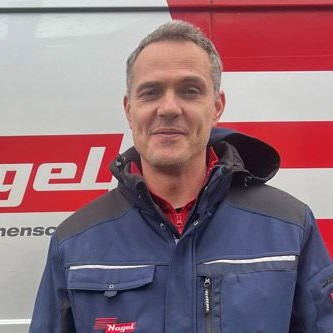 Ein Mann in einer blauen Jacke steht vor einem Nagelwagen.