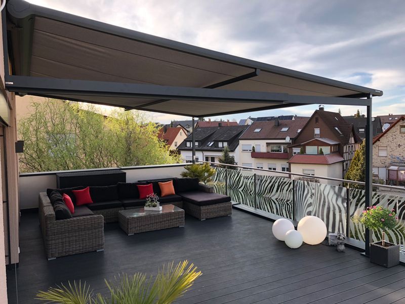 Ein Balkon mit Couch, Tisch, Stühlen und Baldachin.