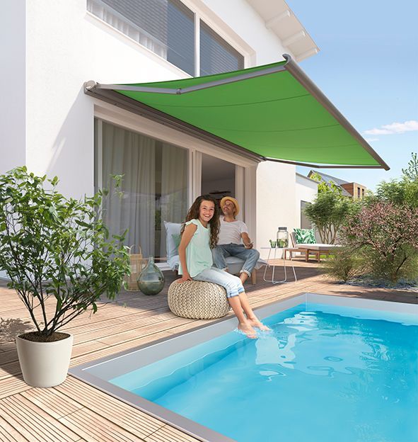 Ein Mann und eine Frau sitzen unter einem Sonnensegel neben einem Swimmingpool.