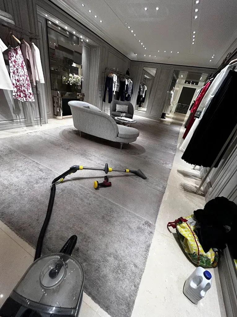 Una limpiadora de alfombras está en funcionamiento en una tienda de ropa de diseñador. Al fondo hay un sofá gris.