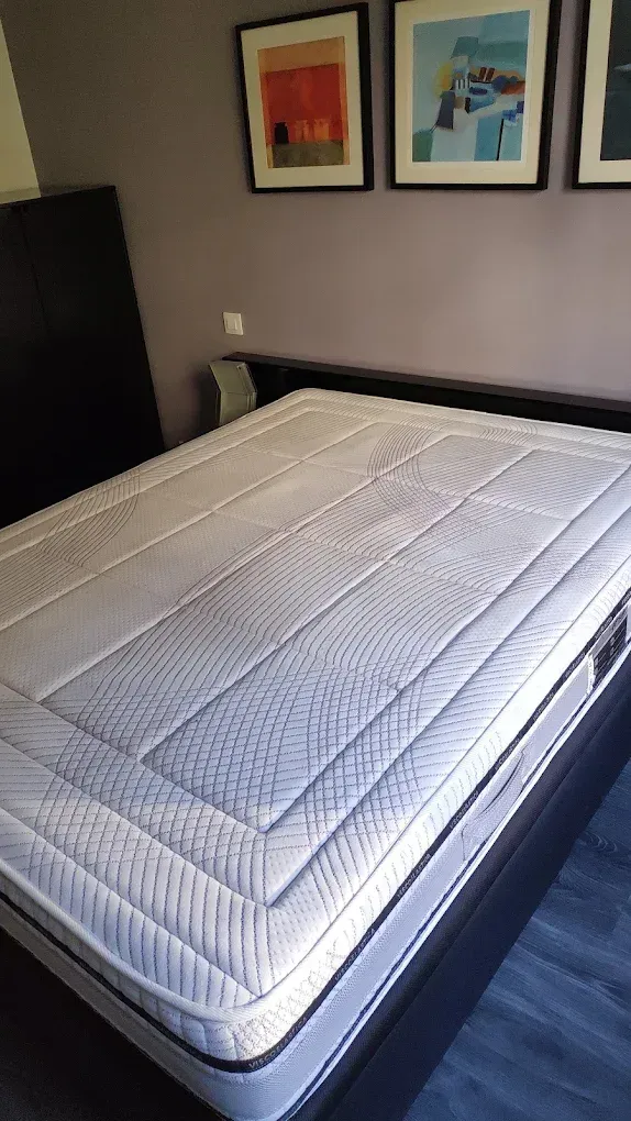 Cama tamaño queen con colchón blanco, marco negro, contra una pared violeta con obras de arte enmarcadas.