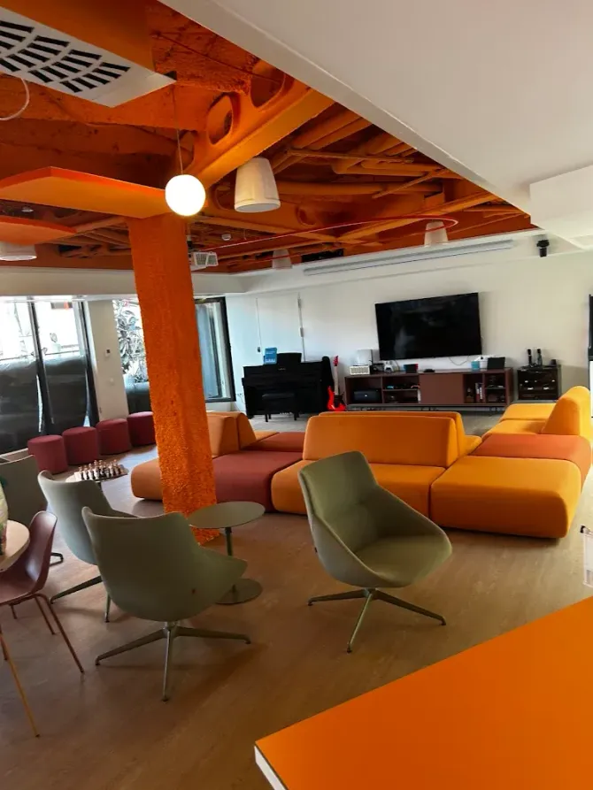 Una moderna sala de estar con asientos modulares de color naranja, sillones verdes y una estructura de techo naranja con un piano negro.