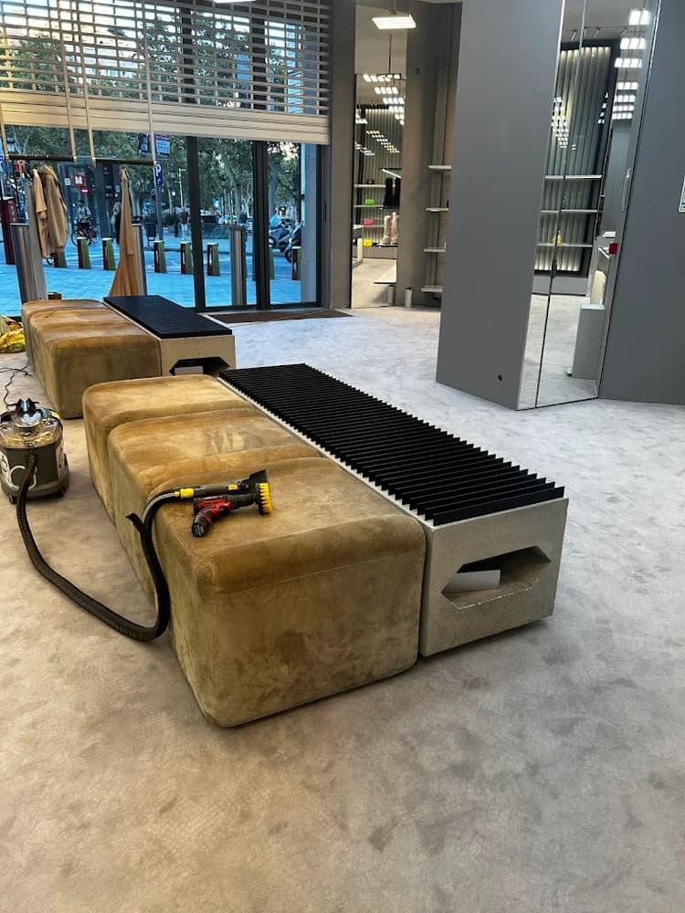 Un banco color canela con un limpiador de alfombras en una tienda. Al fondo, paredes grises, una ventana y estanterías.