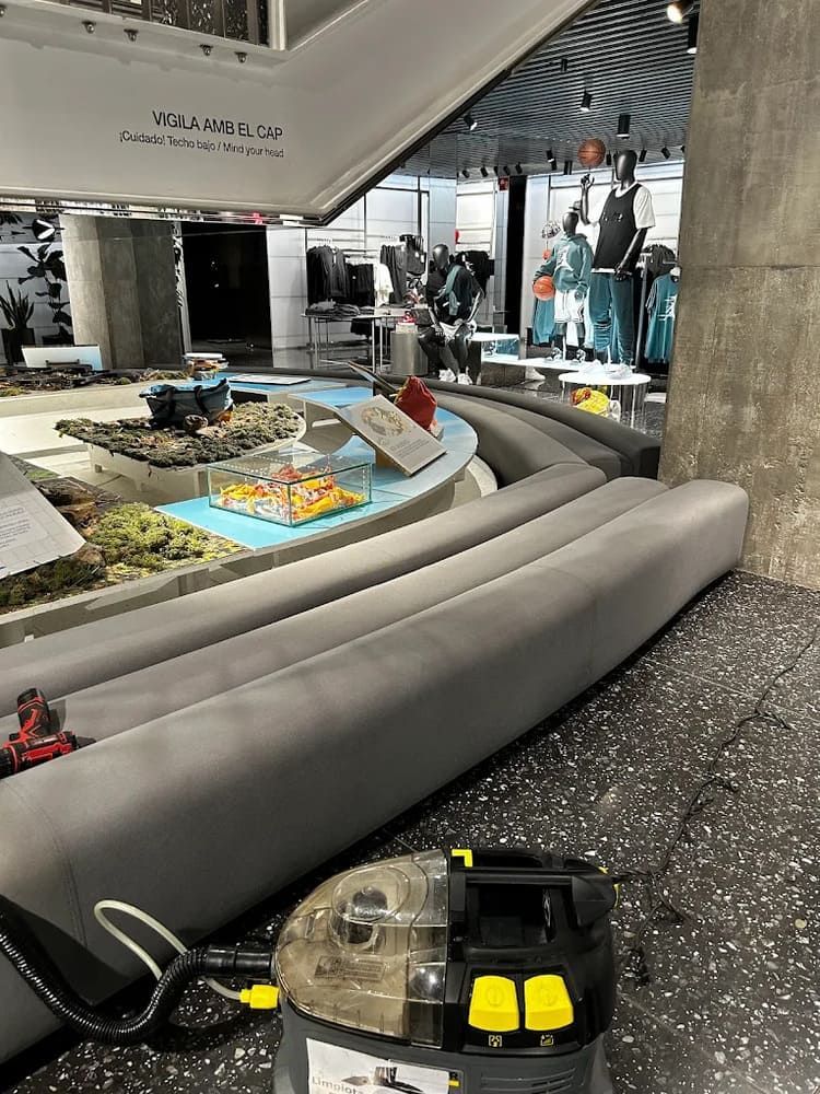 Interior de una tienda con una aspiradora cerca de una zona de asientos curva y expositores.