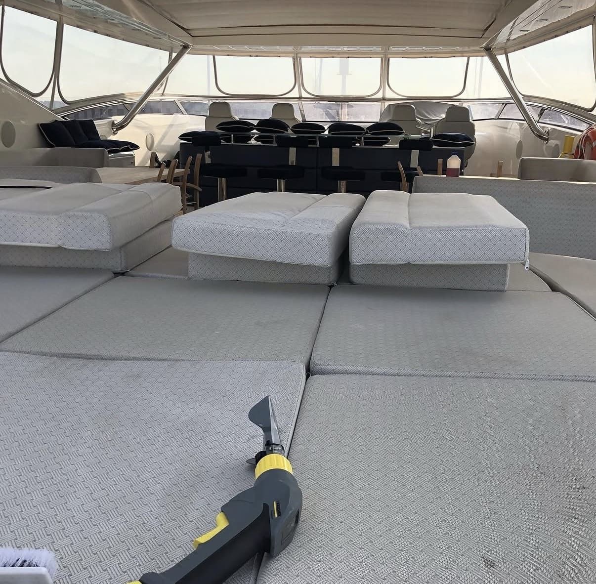 Una herramienta de medición láser portátil descansa sobre cojines grises de exterior a bordo de un yate, con asientos en la cubierta al fondo.