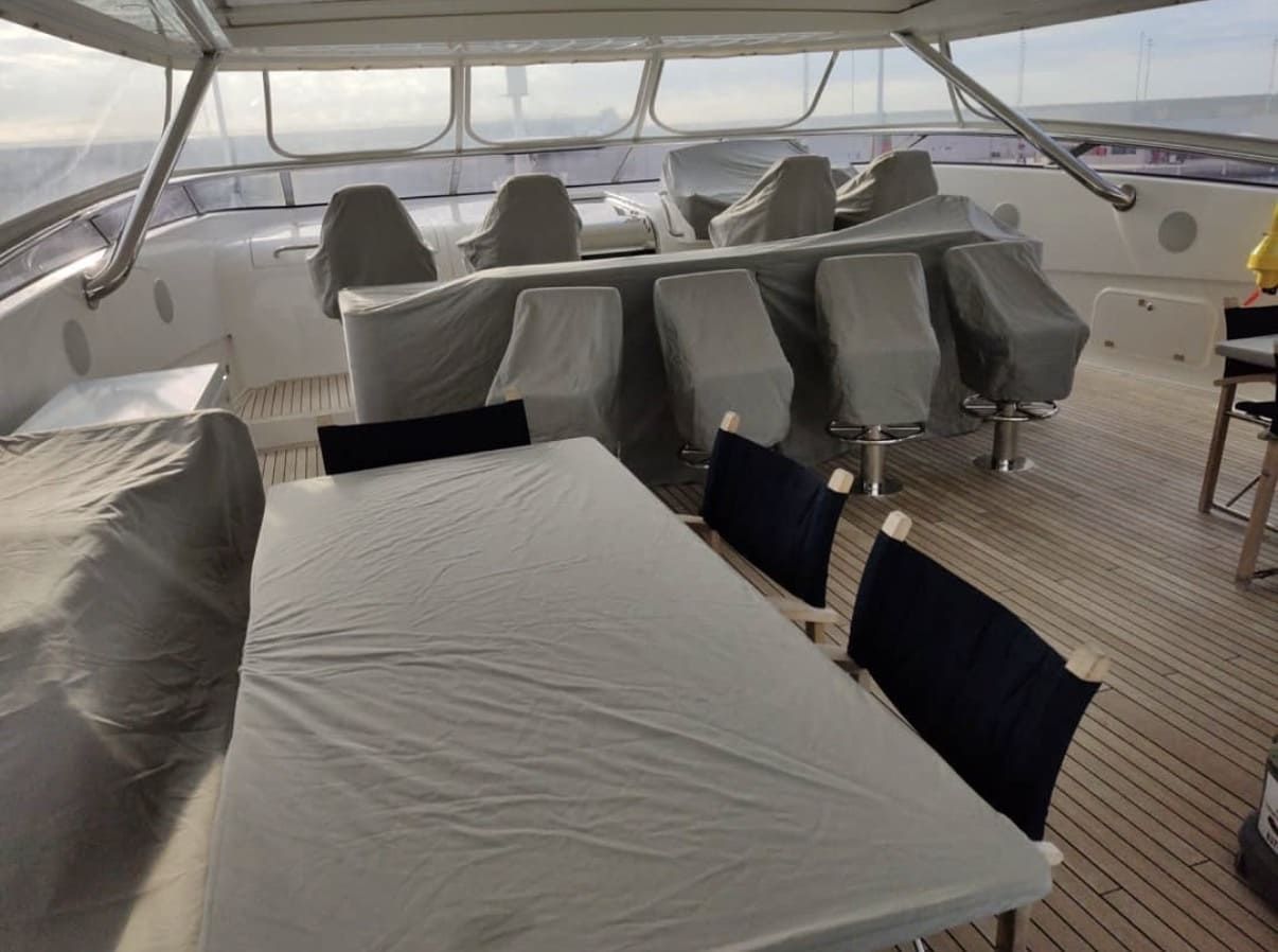 La cubierta exterior de un yate cuenta con una mesa de comedor cubierta, sillas azul marino, asientos acolchados y vistas panorámicas al mar.