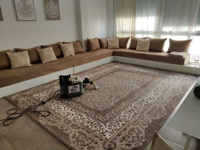 Una máquina de limpieza de alfombras descansa sobre una alfombra grande y estampada en una sala de estar con sofás modulares de color beige.