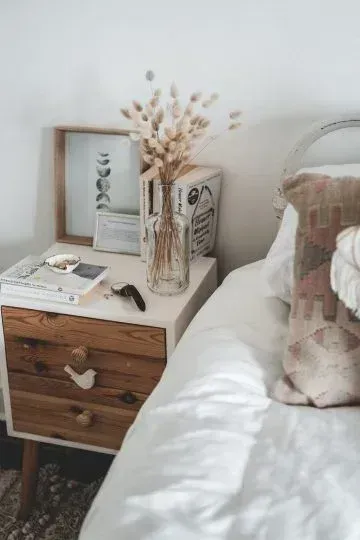 Un dormitorio con una cama, mesita de noche y jarrón de flores.