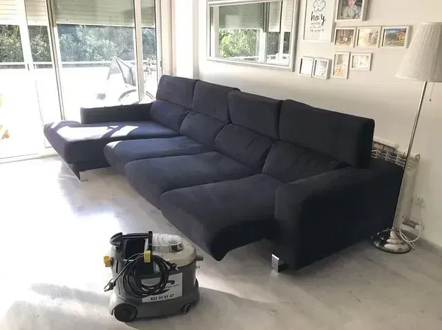 Un gran sofá azul está sentado en una sala de estar al lado de una aspiradora.