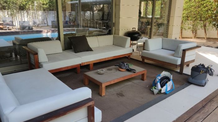 En la zona del patio hay un gran conjunto de sofás de madera de color claro con cojines blancos alrededor de una mesa de centro a juego.