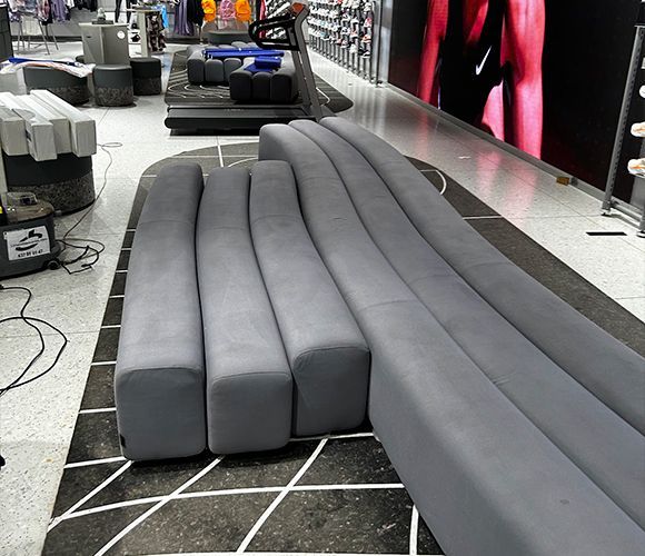 Asientos curvos de color gris en una tienda minorista, colocados sobre una alfombra estampada.