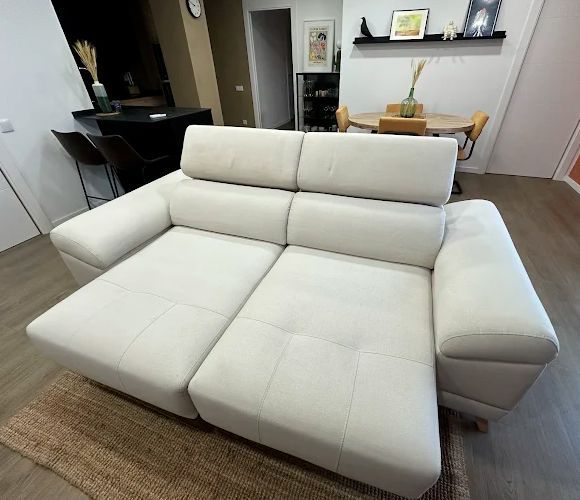 Sofá color crema en una sala de estar, con una cocina y un comedor al fondo.