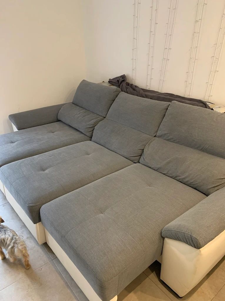 Sofá seccional gris y blanco en una habitación, con un perro pequeño en primer plano.