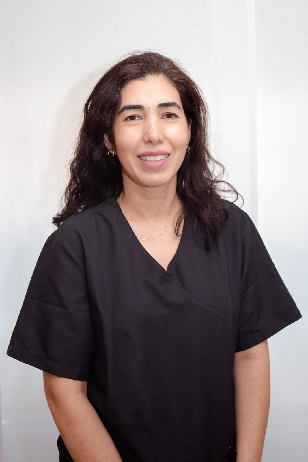 Persona con uniforme médico negro de pie y sonriendo contra un fondo claro.