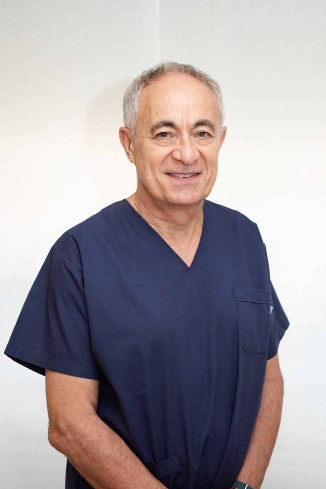 Persona vestida con uniforme médico azul marino, de pie y sonriendo contra un fondo claro liso.