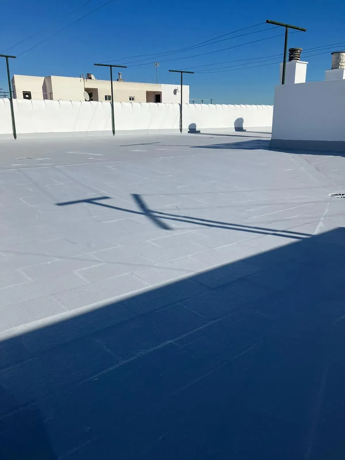 Techo blanco con postes altos que proyectan largas sombras bajo un cielo azul claro y brillante.