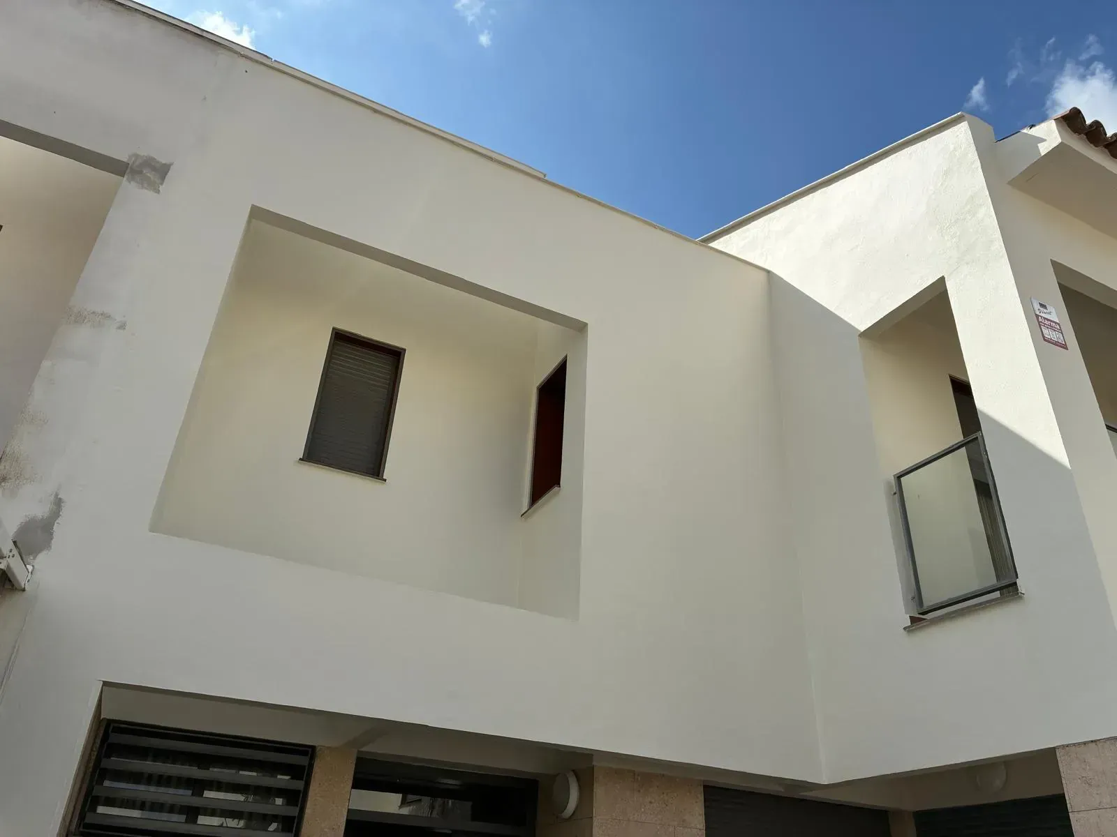 Edificio blanco con recortes rectangulares para ventanas y un balcón contra un cielo azul.