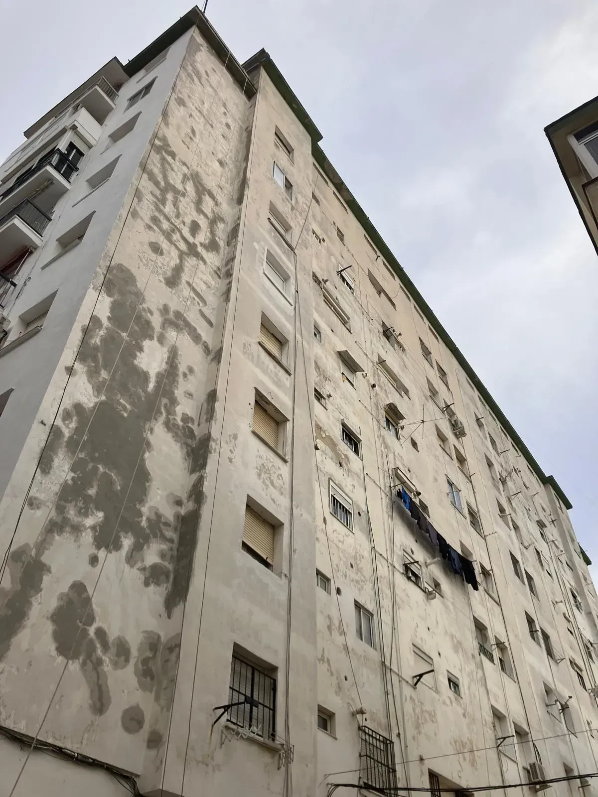 Edificio de apartamentos alto y blanco con pintura descascarada; cielo nublado.