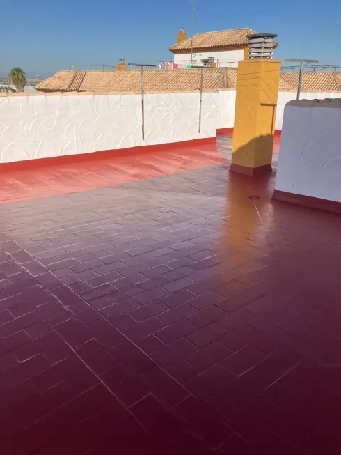 Tejado de tejas rojas con paredes blancas y una chimenea amarilla bajo un cielo azul.
