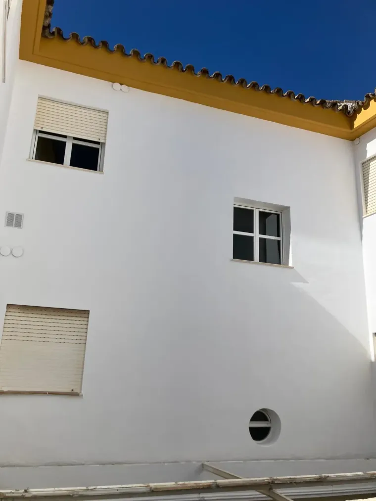 Exterior de edificio blanco con varias ventanas, molduras amarillas y cielo azul.