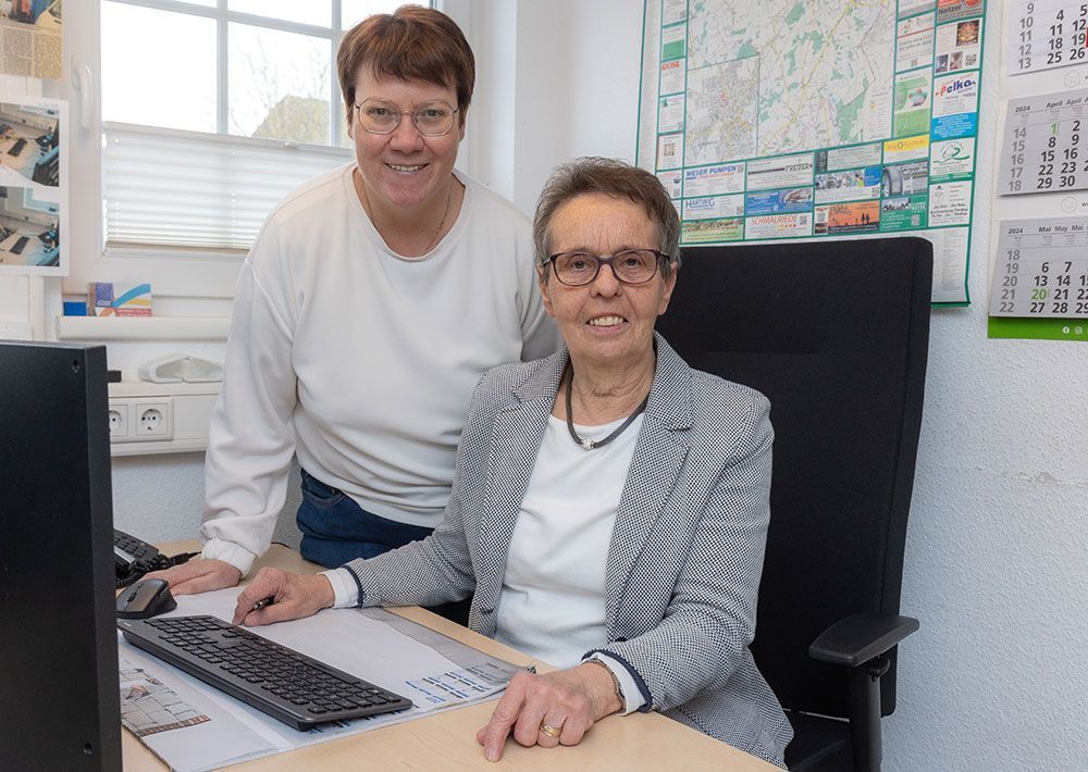 Zwei Frauen sitzen an einem Schreibtisch vor einem Computer.