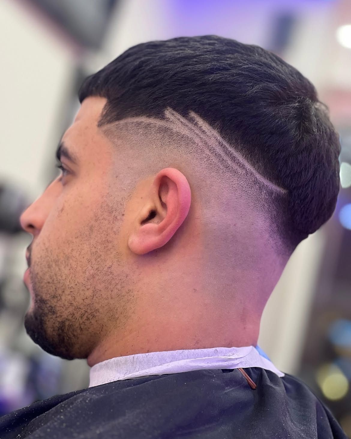 Vista lateral del corte degradado recién hecho de un hombre sentado en una silla de barbero, con un diseño de líneas