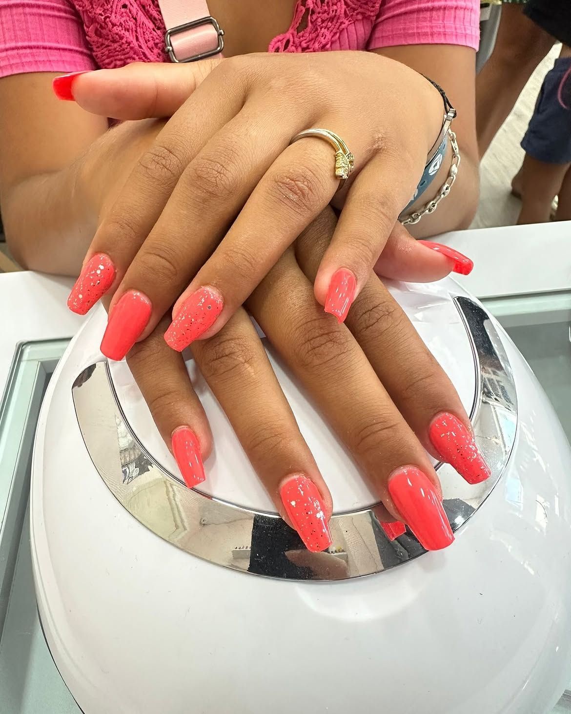 Manos con las uñas de color rosa intenso apoyadas sobre un secador de uñas en un salón de belleza.