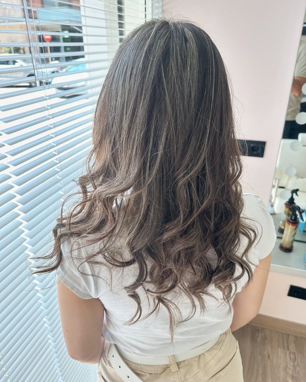 Vista trasera de una mujer con el pelo largo, ondulado y castaño, que lleva una blusa blanca en el interior