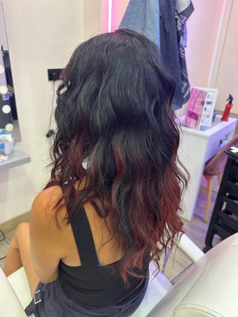 Persona de pelo largo, oscuro y ondulado sentada en una silla de peluquería, vista desde atrás.