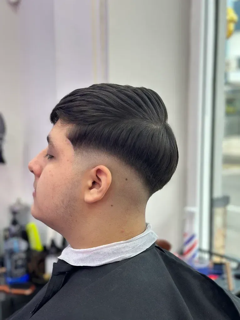Perfil de un hombre con un elegante corte degradado negro, sentado en la silla de una barbería