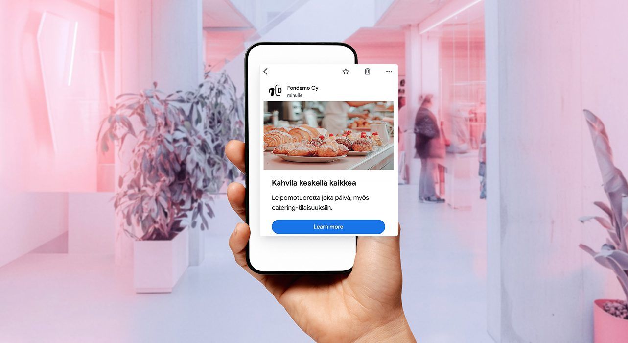 Kädessä on älypuhelin, jossa näkyy sosiaalisen median ponnahdusikkuna, jossa on kuva leivonnaisista tyyliteltyä vaaleanpunaista taustaa vasten.