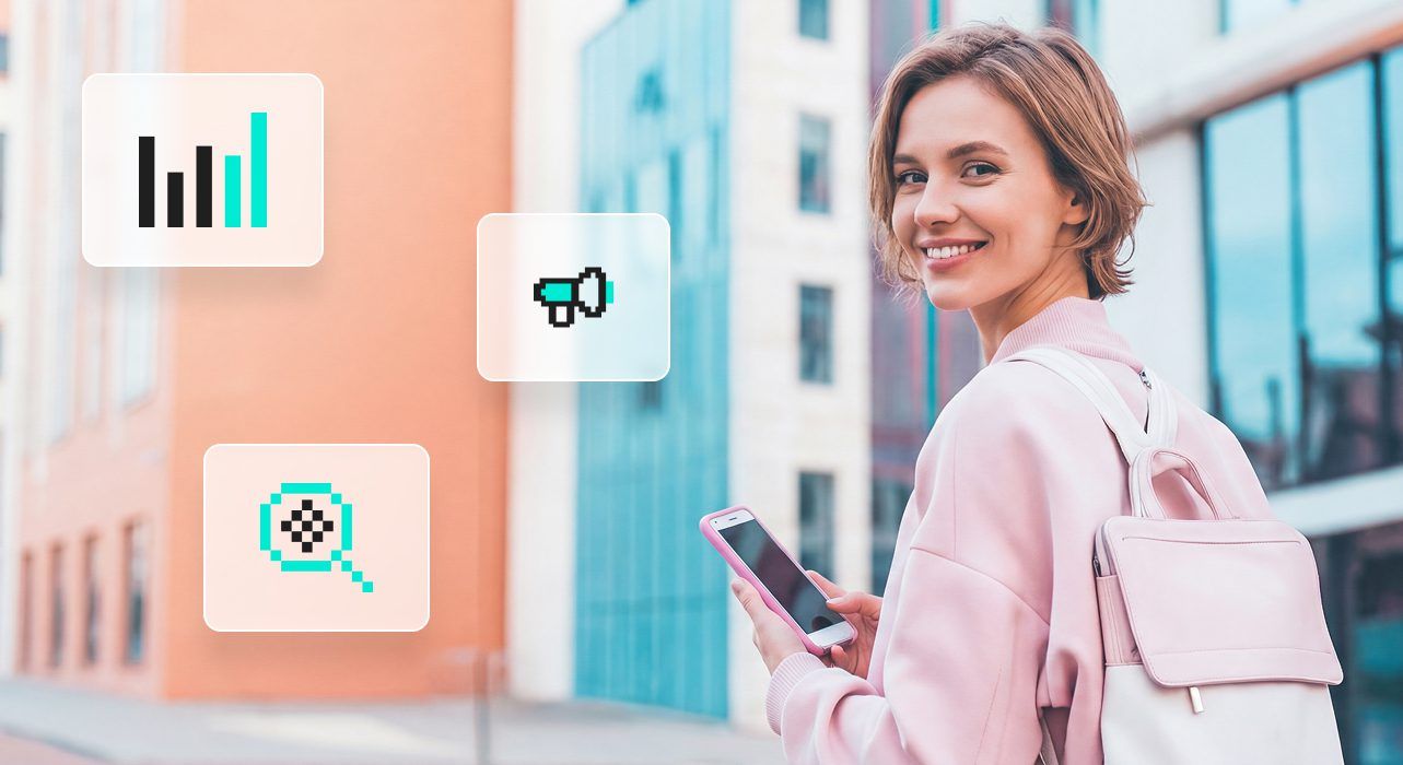 Ihminen hymyilee pitäen älypuhelinta kädessään modernin rakennuksen edessä, jonka päällä on digitaalisia kuvakkeita datalle ja medialle.