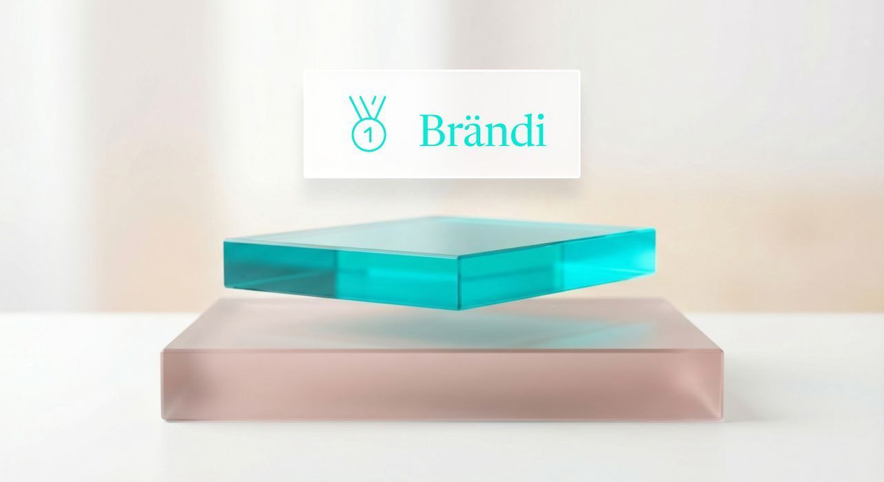 Sinivihreä lasinen neliö leijuu kiinteän, punertavan jalustan yläpuolella vaaleaa taustaa vasten, jossa on Brändi-logo.