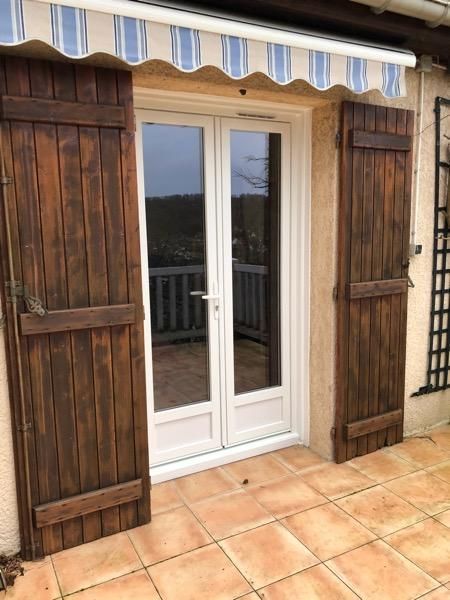 Portes-fenêtres blanches à double vitrage avec volets en bois foncé donnant sur une terrasse carrelée.