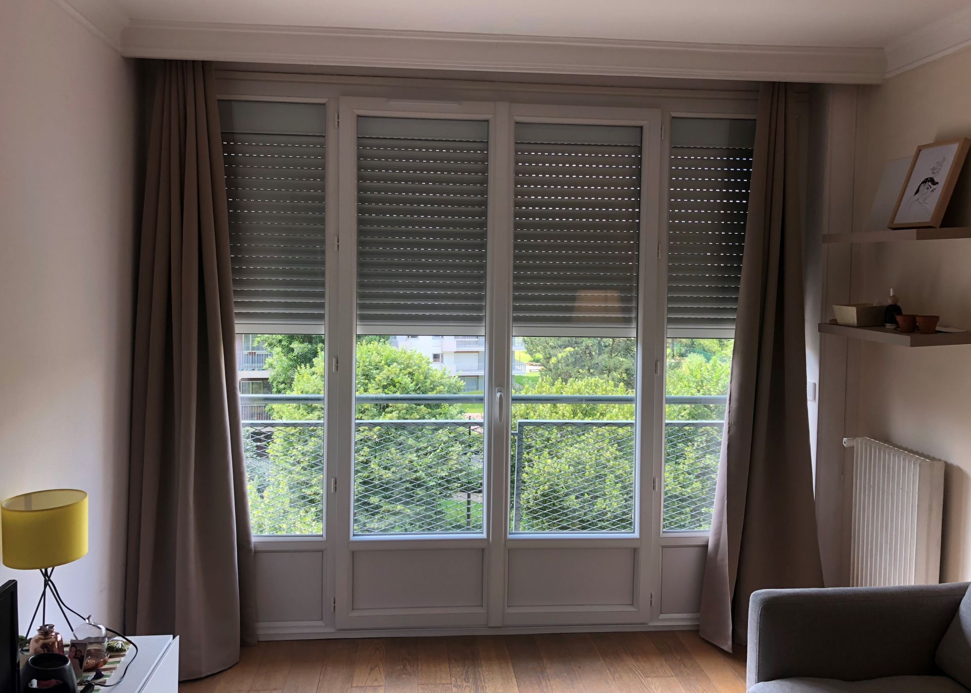 Des rideaux beiges allant du sol au plafond encadrent une grande porte-fenêtre donnant sur un balcon.