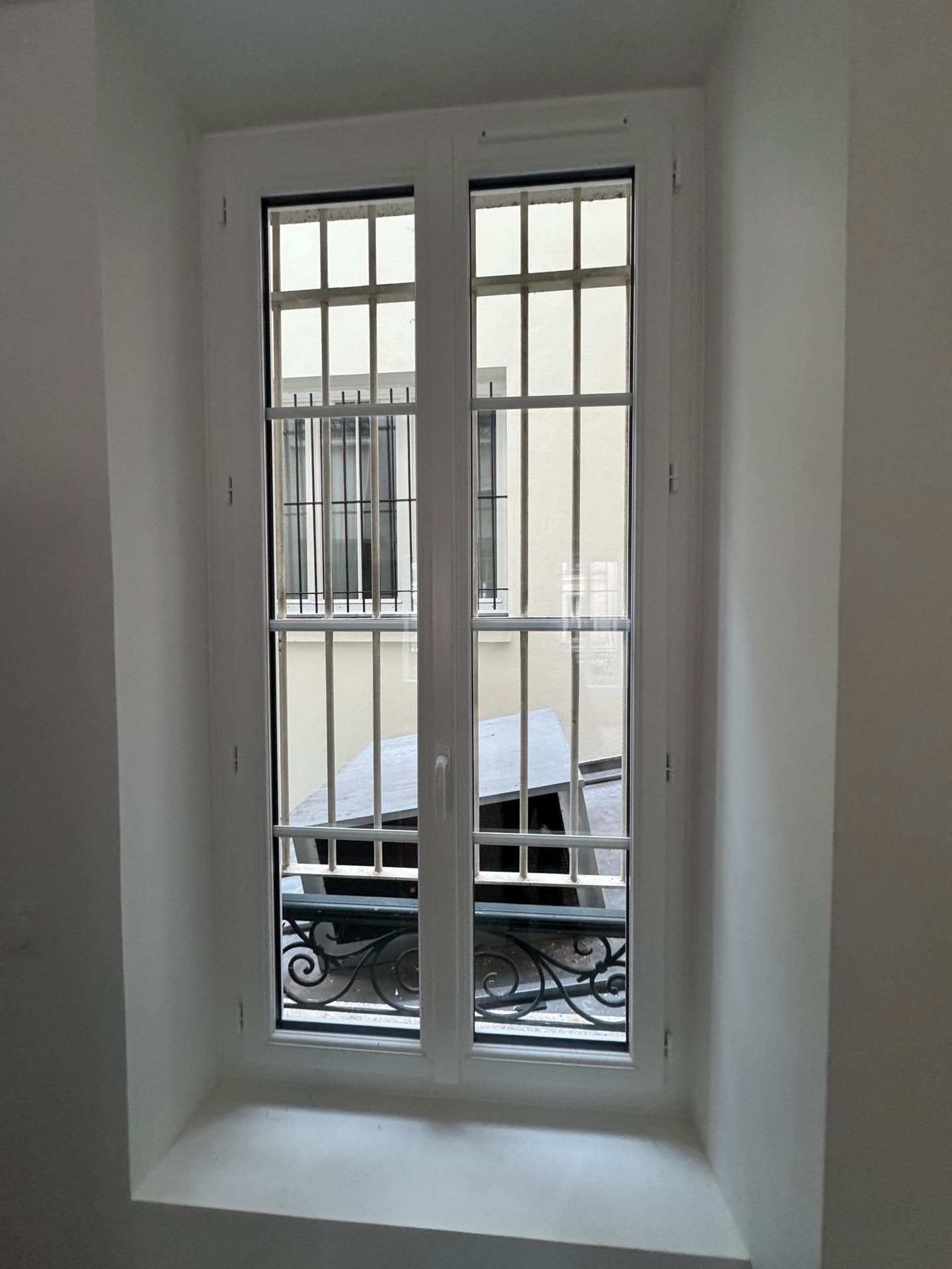 Une fenêtre blanche à double vitrage à motifs quadrillés, encastrée dans un mur blanc épais.