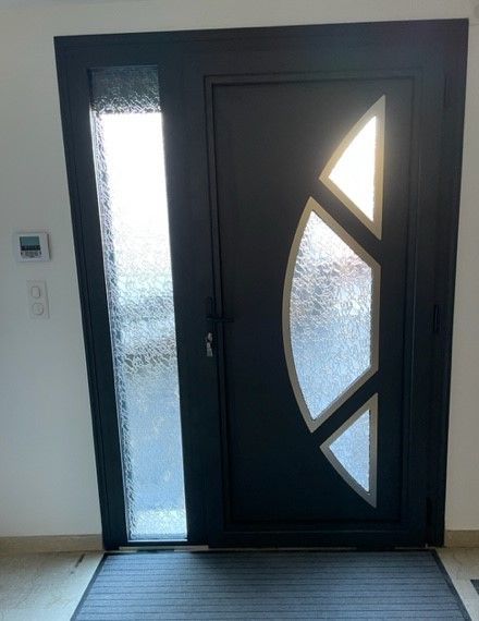 Porte d'entrée moderne noire avec panneaux en verre dépoli et fenêtres latérales géométriques dans un couloir