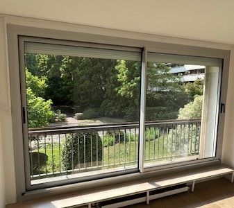 Grande fenêtre donnant sur un jardin verdoyant et une balustrade de balcon.